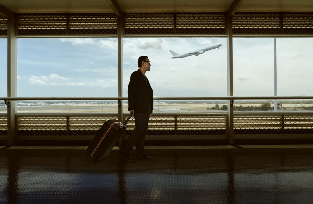 Executive traveler walking with luggage inside Miami International Airport terminal with an airplane taking off in the background